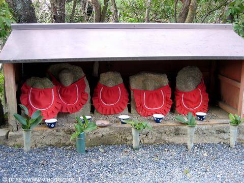 Santuario con pietre avvolte in grembiuli rossi, offerte di tazze e piante, Miyajima