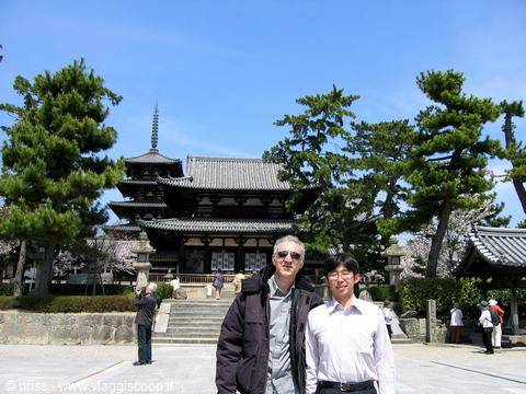 Two men in front of a wooden Buddhist temple with pagoda among pines