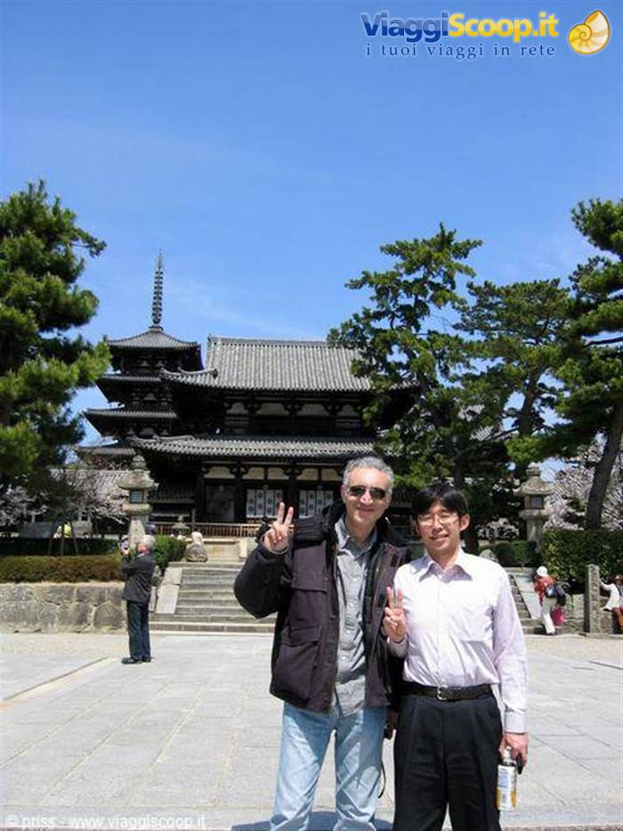 Two men making peace signs before wooden temple hall and pagoda under blue sky