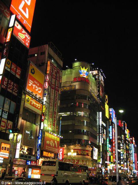 Illuminated neon signs at night in Shinjuku, Tokyo, with skyscrapers and a bus