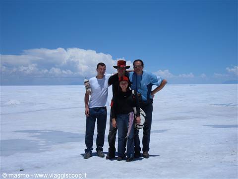 Four friends pose on the white salt of Salar de Uyuni under a blue sky