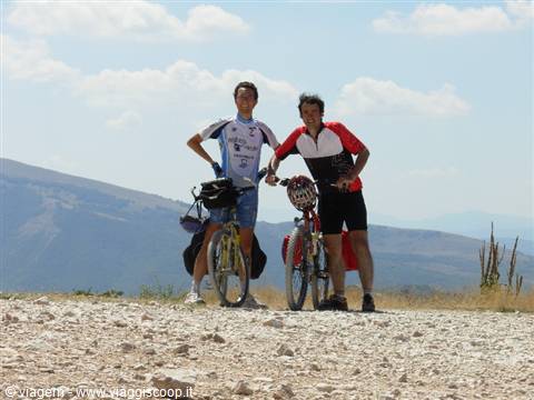 Two cyclists in jerseys stop their bicycles on a rocky mountain trail
