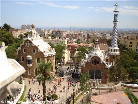 Stone pavilions with white wavy roofs at Park Güell, tourists below the mosaic tower