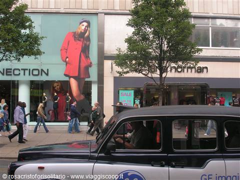 Black taxi cab passing Debenhams store on a busy shopping street