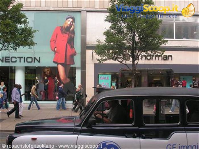 Black taxi cab passing Debenhams store on a busy shopping street