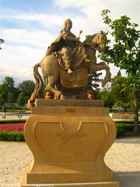 Stone equestrian statue in a garden, a person peeks from behind the pedestal