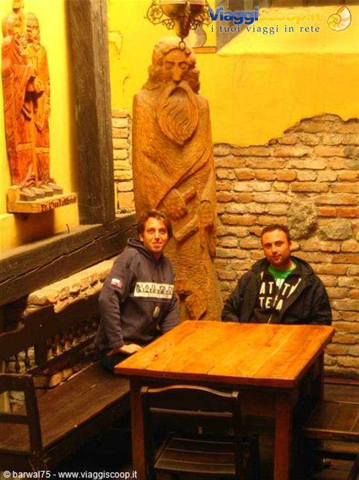 Two young men sitting at a wooden table beside a carved wooden statue