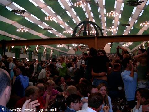 Cheering crowd under green striped tent with chandeliers, beer hall celebration