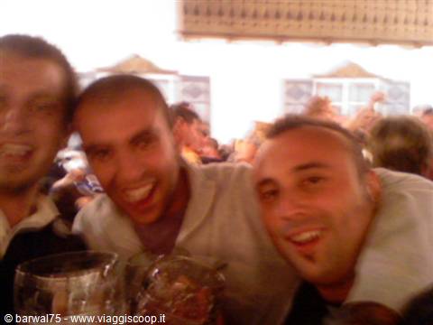 Three smiling friends raising beer steins in a crowded beer hall