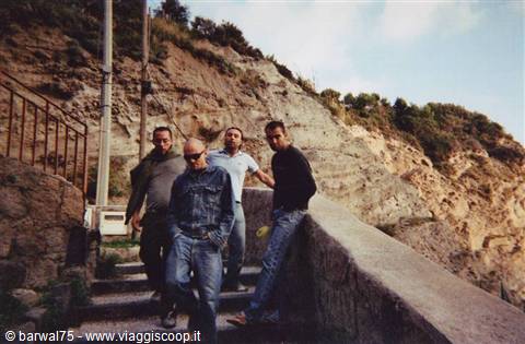 Four friends walking down stone steps beside rocky cliff and greenery, daylight