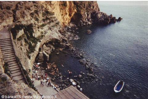 Stone staircase descends to rocky cove with swimmers and a blue boat