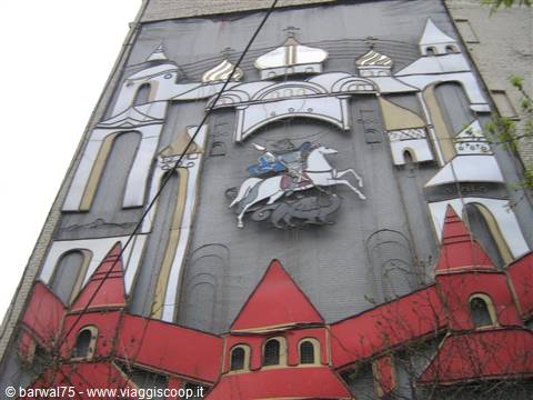 Metal mosaic on building facade: horseman slaying the dragon, red towers