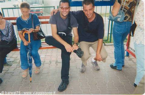 Two young men crouching and smiling at a bus stop with wooden benches