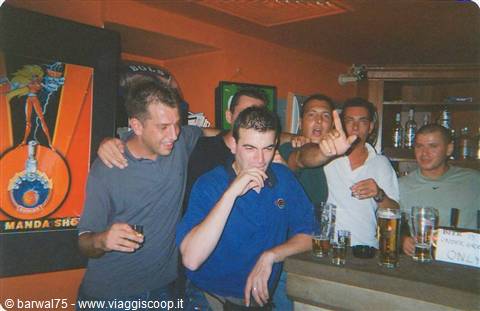 Group of friends at a pub with beer glasses, one making hand gesture