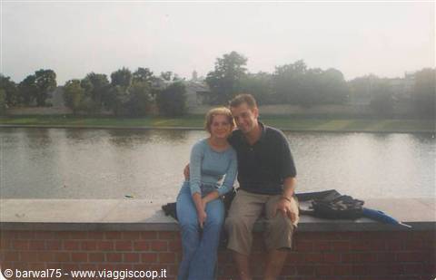 Couple sitting on a brick wall beside a river with trees behind