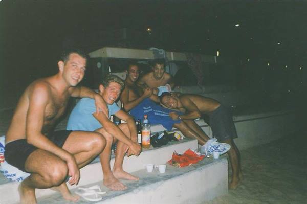 Group of friends in swimwear on concrete steps by the beach at night
