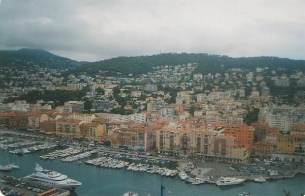 Nice harbor: moored yachts, ochre buildings, green hill under cloudy sky