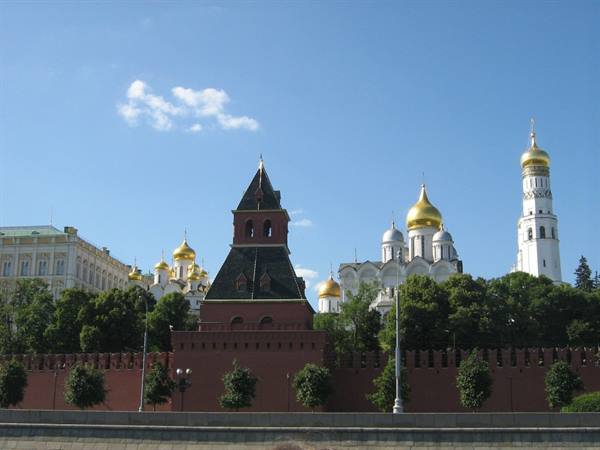 Red Kremlin walls in Moscow with golden domes and bell tower under blue sky