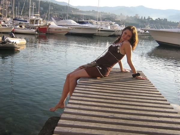 Girl in brown dress posing on wooden pier among yachts in marina