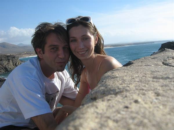 Smiling couple leaning on volcanic rock by the sea, blue sky