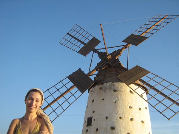 Smiling woman beside an old whitewashed cylindrical windmill under blue sky
