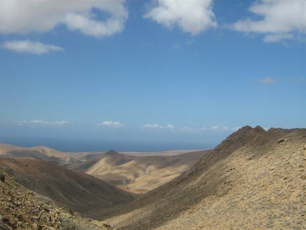Arid rocky volcanic hills under a blue sky with clouds
