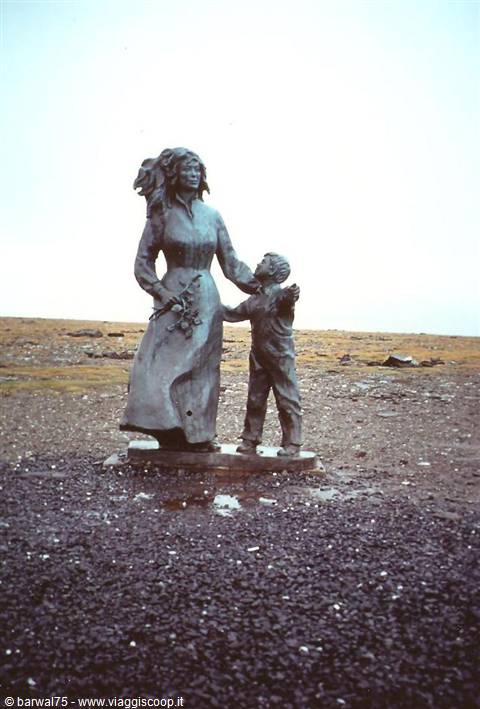 Bronze statue of a woman and child on barren tundra under gray sky