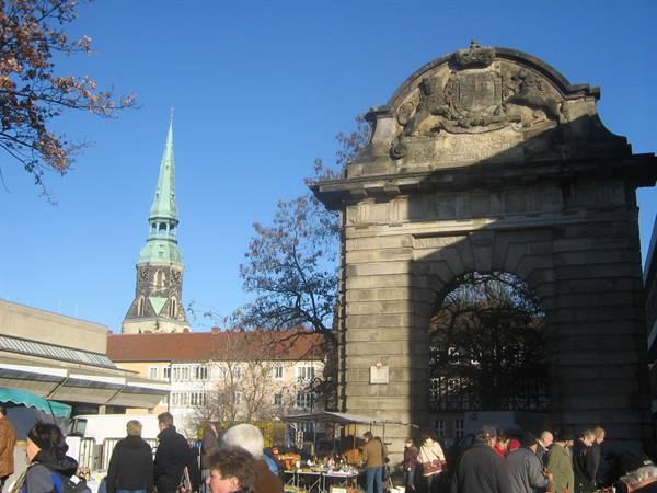 Stone gate with carved crest, market crowd, church spire with green patina