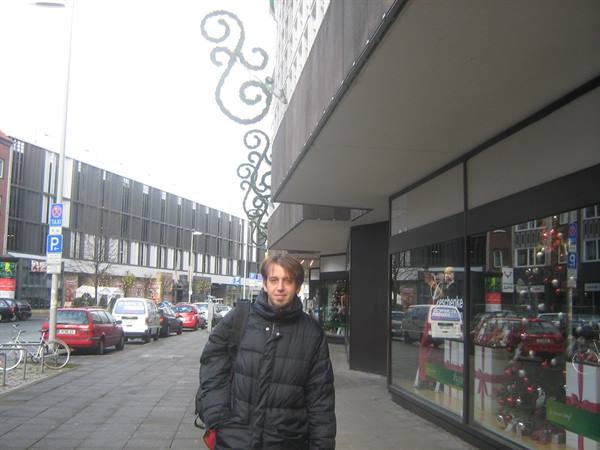 Man in black puffer jacket walks along sidewalk past decorated shop windows