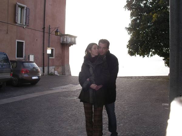 Couple embracing on cobblestones by the lake, bright light near painted houses