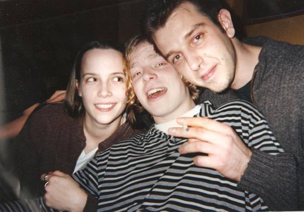 Three friends huddled together, one holding a cigarette, dim flash lighting