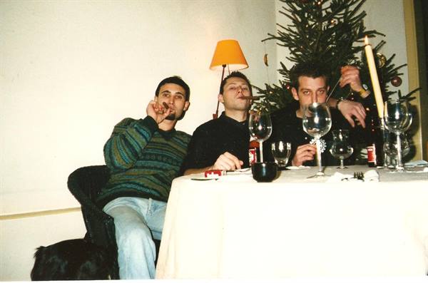 Three friends smoke and drink wine at a table by the Christmas tree