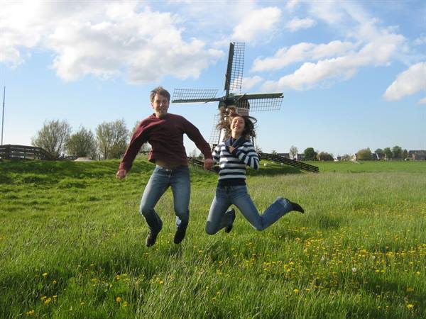 Couple jumping in a flowered meadow in front of a windmill