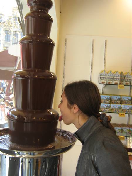 Girl licking melted chocolate from a multi-tier chocolate fountain inside the shop