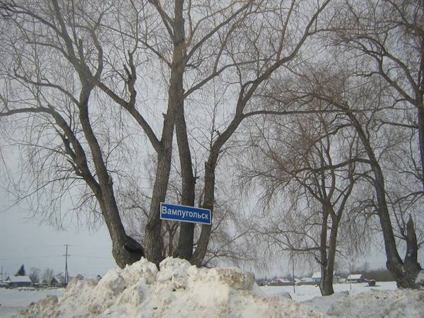 Blue Vampugolsk village sign among bare trees and piled snow
