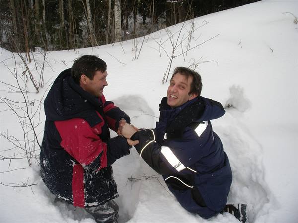 Two men in winter jackets play in deep snow among trees