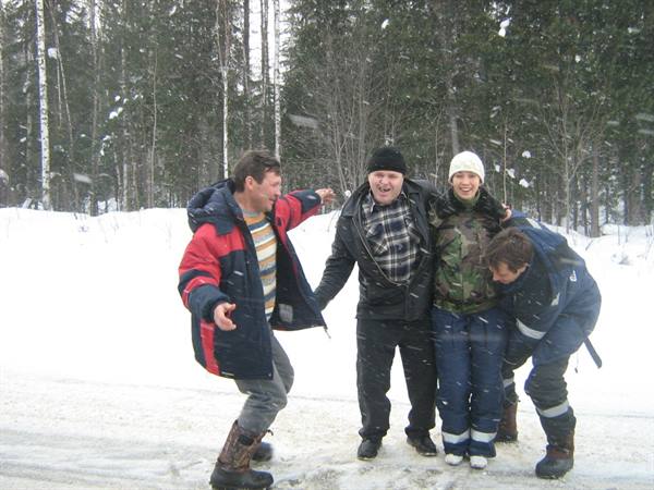 Four friends laughing and joking in the snow, birch forest behind them