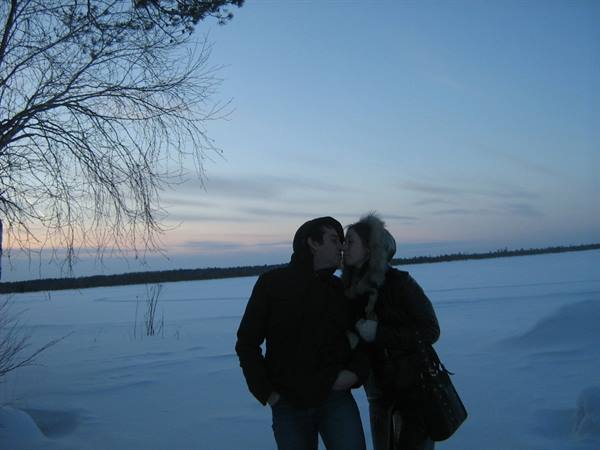 Couple kissing beside a bare tree on snow at dusk