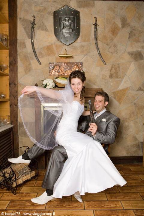 Bride and groom posing indoors, stone wall decorated with swords and shield