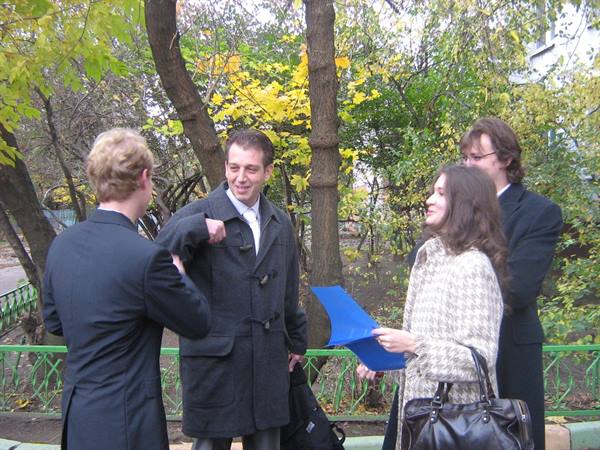 Four young people in coats chat in an autumn park, woman holding blue folders