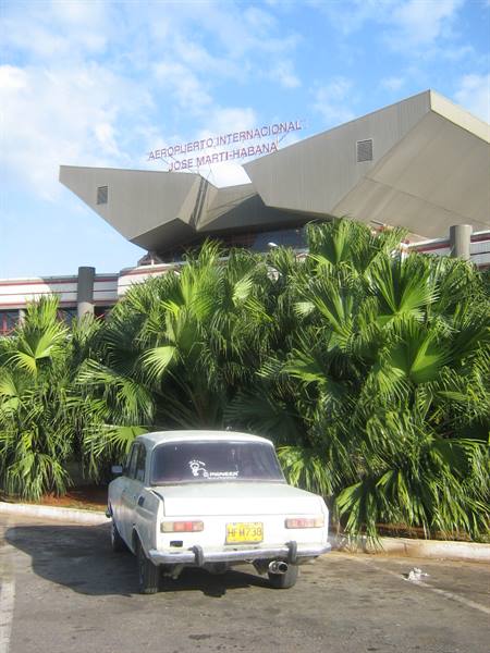 White car parked in front of José Martí airport, green palms, blue sky