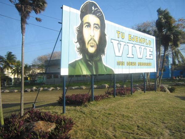 Billboard with Che Guevara portrait reading Vive among palm trees