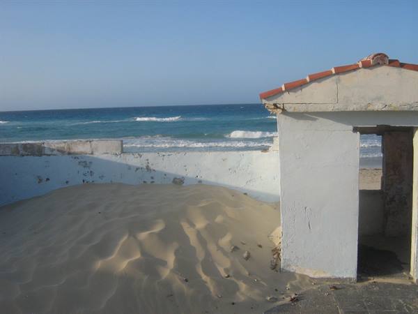Sand invades an old white building with tiled roof by the sea