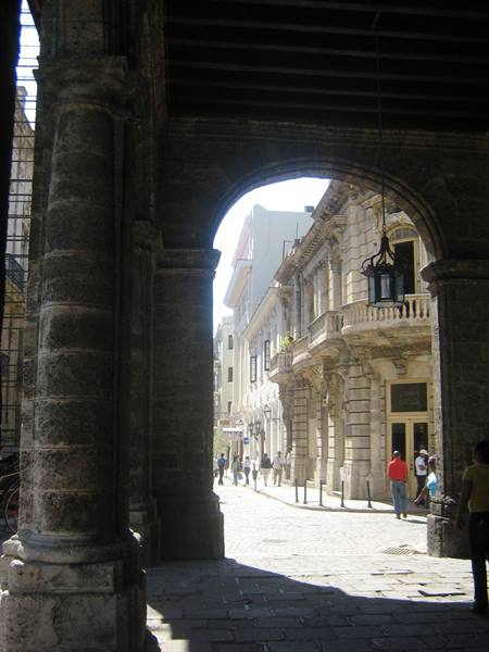 Stone archway with hanging lantern, pedestrians on cobbled street among colonial buildings, Havana