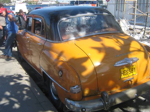 Vintage yellow car with black roof, plate HES581, parked in shade in Havana