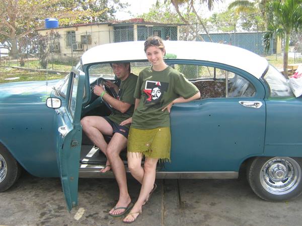 Woman in green t-shirt leaning on a blue vintage car, man at the wheel