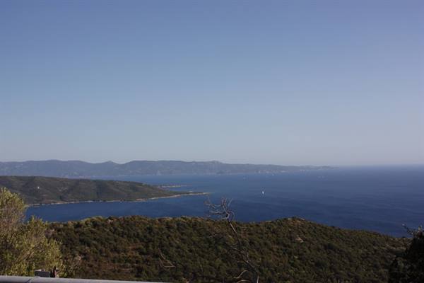 Deep blue sea between shrubby hills and distant coastline, clear sky, a sailboat