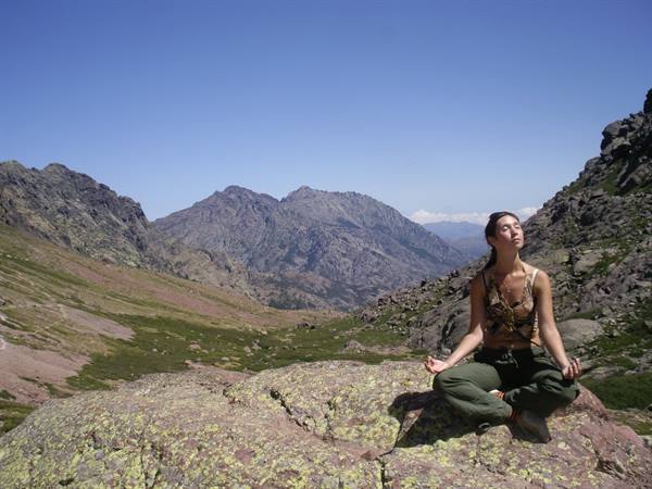Woman sits cross-legged meditating on a lichen-covered rock among granite mountains