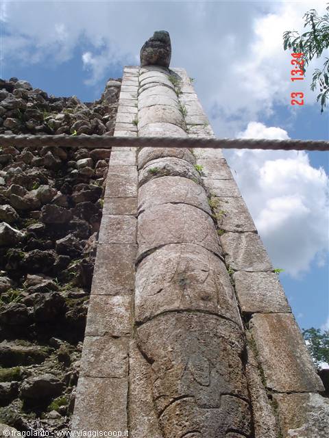 Carved stone column with serpent head, Mayan ruins beneath blue sky