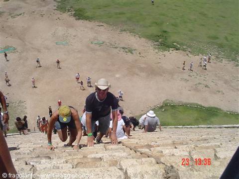 Tourists climb steep ancient stone pyramid steps under bright daylight
